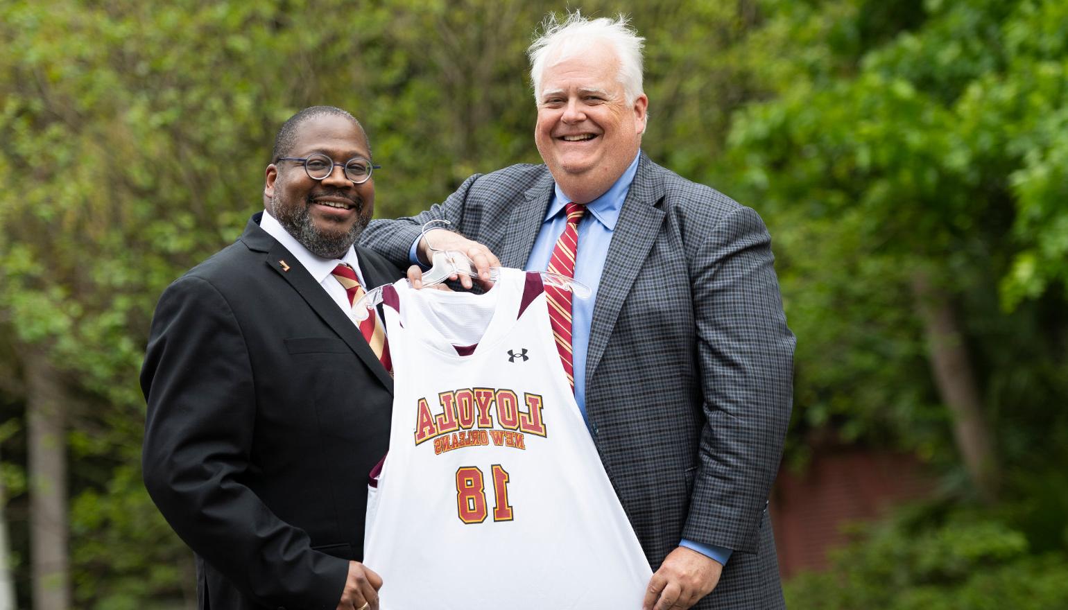 Stephen Landry '83, chair of the Board of Trustees, presents Dr. Xavier Cole with a #18 basketball jersey